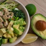 Delicious vegan bowl with zoodles, avocado, tofu, and greens on a wooden table.