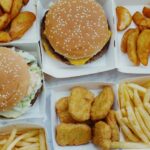 Top view of yummy junk food consisting of burgers and french fries with nuggets placed in boxes on marble background