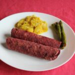 A delightful vegan dish featuring asparagus, curry, and beetroot rolls on a vibrant pink surface.