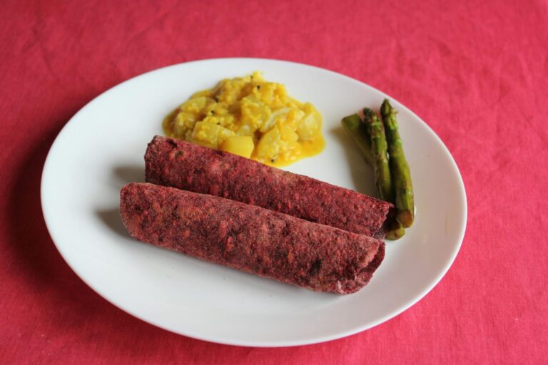 A delightful vegan dish featuring asparagus, curry, and beetroot rolls on a vibrant pink surface.